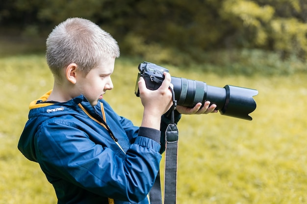 Junger kaukasischer Junge, der ein Schießen mit seiner DSLR-Kamera macht. Naturumgebung.