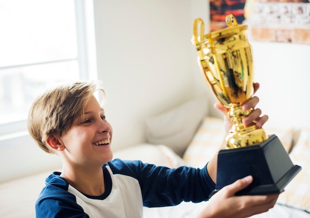 Junger kaukasischer Junge, der fröhliches Glück der Trophäe hält