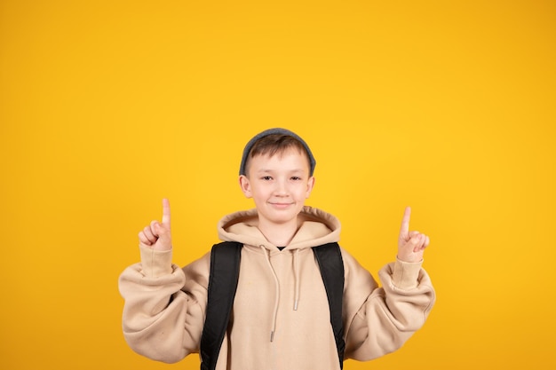 Junger kaukasischer Junge, der vor gelbem Hintergrund steht und aufgeregt ausruft und beide Zeigefinger nach oben zeigt