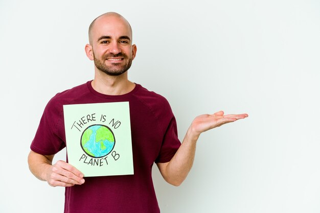 Junger kaukasischer kahlköpfiger Mann, der ein dort ist, ist nicht Planet B Plakat isoliert auf lila Hintergrund, der einen Kopienraum auf einer Handfläche zeigt und eine andere Hand auf Taille hält.