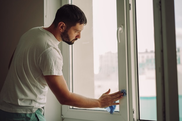 junger kaukasischer lächelnder Mann, der das Fenster mit einem Rakel wäschtReinigungskonzept