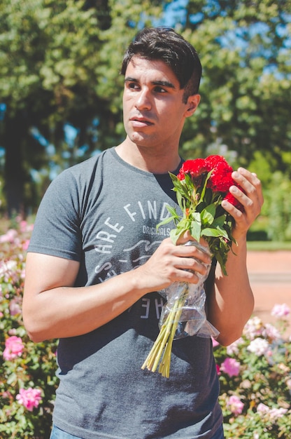 Junger kaukasischer lateinamerikanischer Mann draußen im Park mit einem Blumenstrauß in der Hand