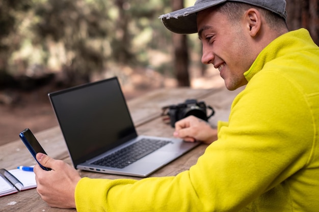 Junger kaukasischer männlicher Freiberufler, der ein Mobiltelefon benutzt, während er an einem Laptop arbeitet