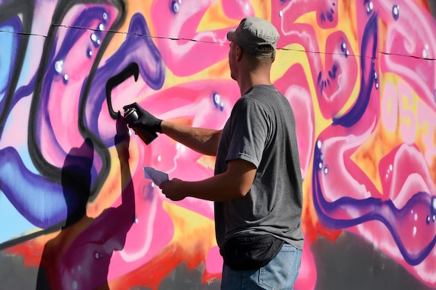 Junger kaukasischer männlicher Graffiti-Künstler, der große Street-Art-Malerei in Blau- und Rosatönen zeichnet