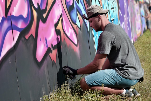 Junger kaukasischer männlicher Graffiti-Künstler, der große Street-Art-Malerei in Blau- und Rosatönen zeichnet
