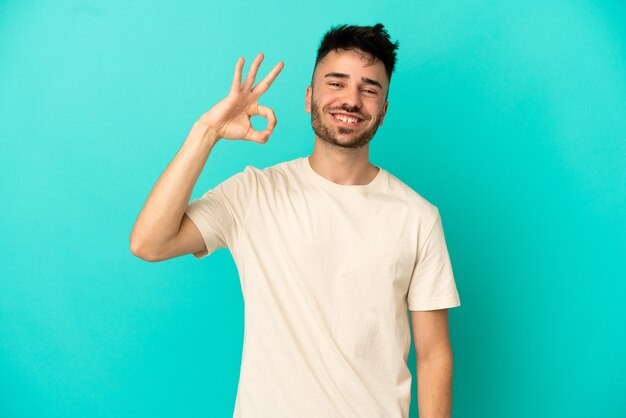 Junger kaukasischer Mann auf blauem Hintergrund isoliert, der ein OK-Zeichen mit den Fingern zeigt