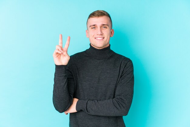 Junger kaukasischer Mann auf einer blauen Wand, die Nummer zwei mit den Fingern zeigt.