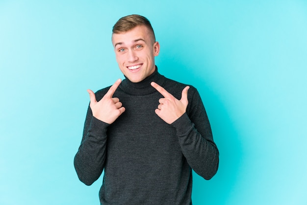 Junger kaukasischer Mann auf einer blauen Wand lächelt und zeigt Finger auf Mund.