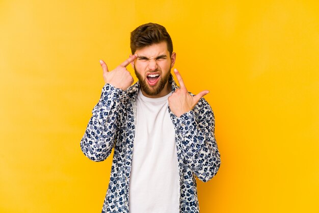 Junger kaukasischer Mann auf gelber Wand, die eine Enttäuschungsgeste mit Zeigefinger zeigt.