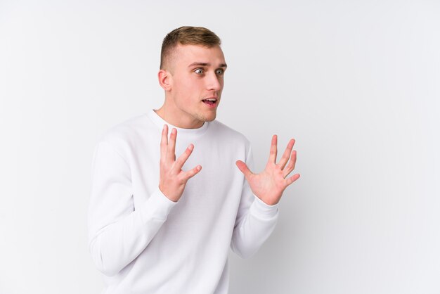 Junger kaukasischer Mann auf weißer Wand schreit laut, hält Augen geöffnet und Hände angespannt.