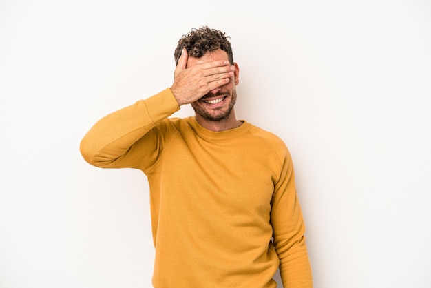 Junger kaukasischer Mann, der auf weißem Hintergrund isoliert ist, bedeckt die Augen mit den Händen, lächelt breit und wartet auf eine Überraschung.