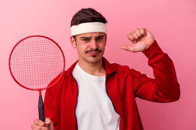 Junger kaukasischer Mann, der Badminton einzeln auf rosafarbenem Hintergrund spielt, fühlt sich stolz und selbstbewusst, Beispiel zu folgen.