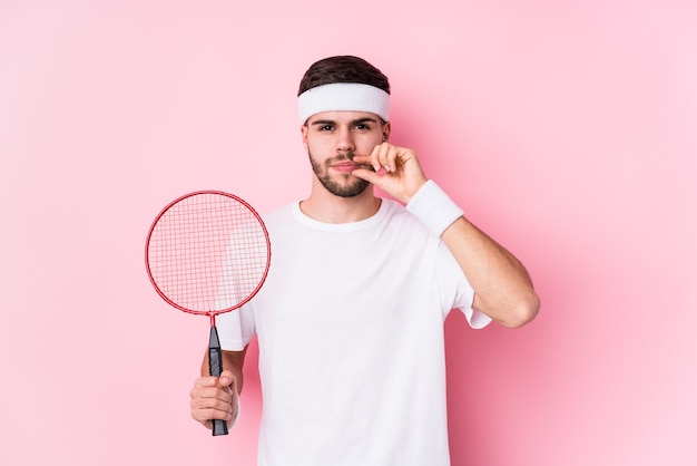 Junger kaukasischer Mann, der Badminton spielt, isoliert mit den Fingern auf den Lippen, die ein Geheimnis halten.