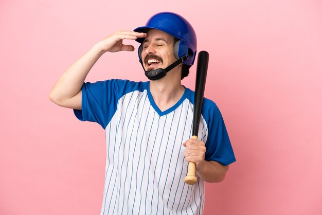 Junger kaukasischer Mann, der Baseball isoliert auf rosa Hintergrund spielt und viel lächelt