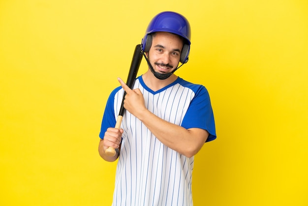 Junger kaukasischer Mann, der Baseball spielt, isoliert auf gelbem Hintergrund, der auf die Seite zeigt, um ein Produkt zu präsentieren