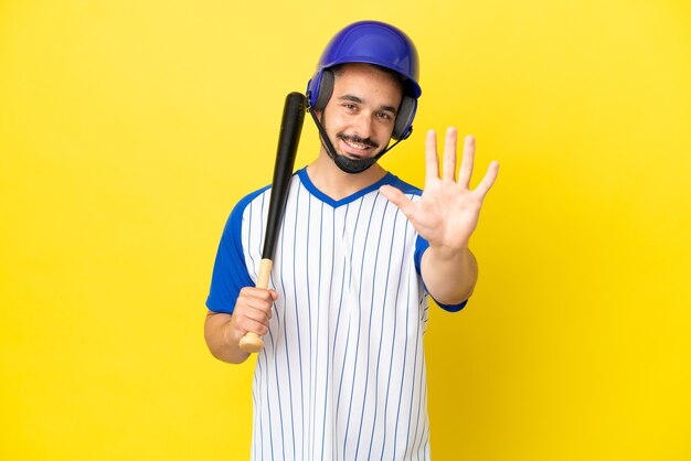 Junger kaukasischer Mann, der Baseball spielt, isoliert auf gelbem Hintergrund, der fünf mit den Fingern zählt