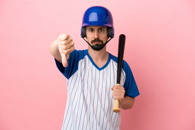 Junger kaukasischer Mann, der Baseball spielt, isoliert auf rosa Hintergrund, der Daumen nach unten mit negativem Ausdruck zeigt