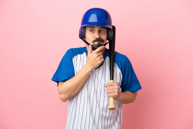 Junger kaukasischer Mann, der Baseball spielt, isoliert auf rosa Hintergrund, der Zweifel hat und denkt