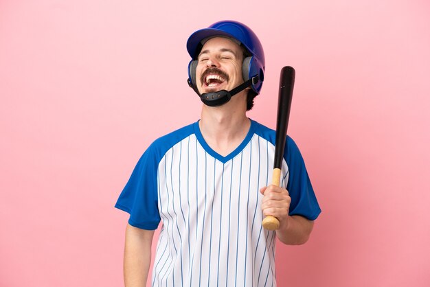 Junger kaukasischer Mann, der Baseball spielt, isoliert auf rosa Hintergrund lachend