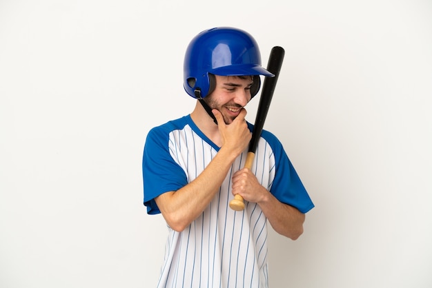 Junger kaukasischer Mann, der Baseball spielt, isoliert auf weißem Hintergrund, der zur Seite schaut und lächelt
