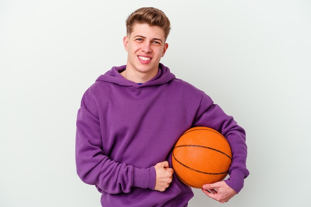 Junger kaukasischer Mann, der Basketball isolierte Wand spielt, lacht und Spaß hat