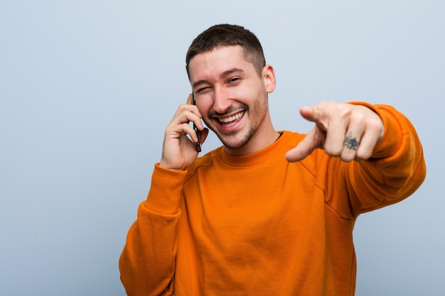 Junger kaukasischer Mann, der ein freundliches Lächeln des Telefons zeigt auf Front hält.
