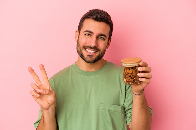 Junger kaukasischer Mann, der ein Mandelglas lokalisiert auf rosa Wand zeigt, die Nummer zwei mit den Fingern zeigt.