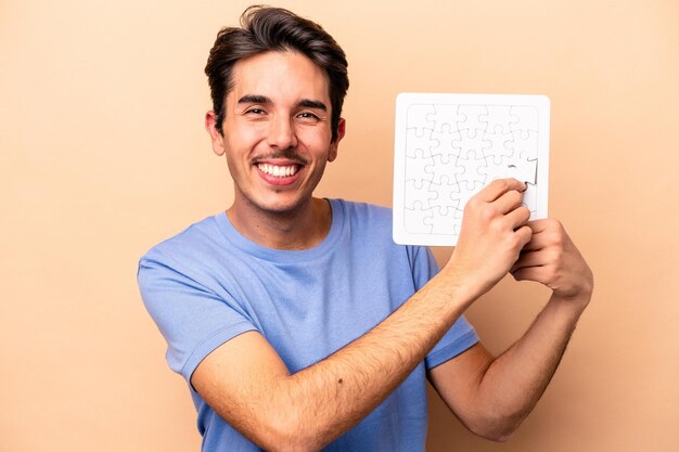 Junger kaukasischer mann, der ein puzzle lokalisiert auf beigem hintergrund hält