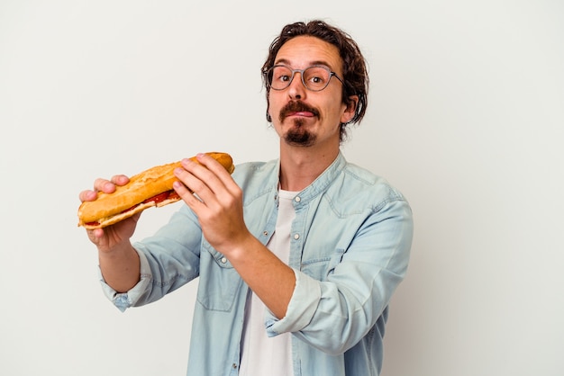 Junger kaukasischer Mann, der ein Sandwich lokalisiert auf weißer Wand hält