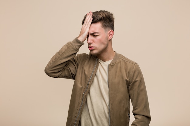 Junger kaukasischer Mann, der eine braune Jacke vergisst etwas trägt, Stirn mit Palme schlägt und Augen schließt.