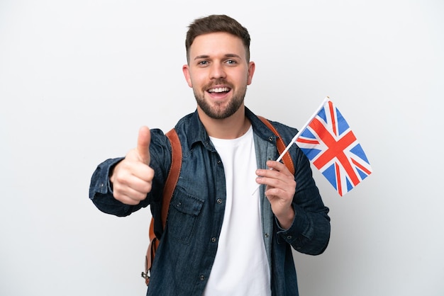 Junger kaukasischer Mann, der eine Flagge des Vereinigten Königreichs isoliert auf weißem Hintergrund mit Daumen nach oben hält, weil etwas Gutes passiert ist