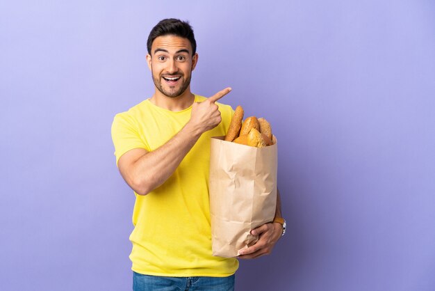 Junger kaukasischer Mann, der eine Tasche voller Brote hält, die auf lila Zeigefinger zur Seite lokalisiert werden