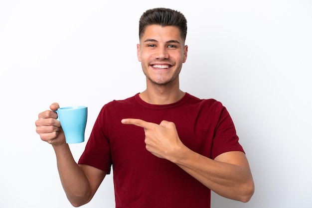 Junger kaukasischer Mann, der eine Tasse Kaffee isoliert auf weißem Hintergrund hält und darauf zeigt