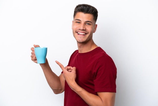 Junger kaukasischer Mann, der eine Tasse Kaffee isoliert auf weißem Hintergrund hält und darauf zeigt