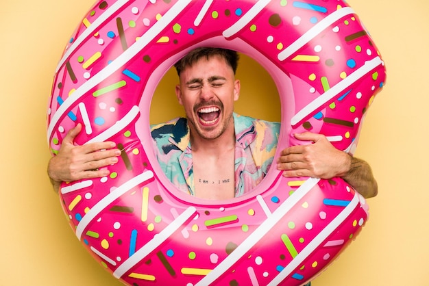 Junger kaukasischer Mann, der einen aufblasbaren Donut hält, isoliert auf gelbem Hintergrund