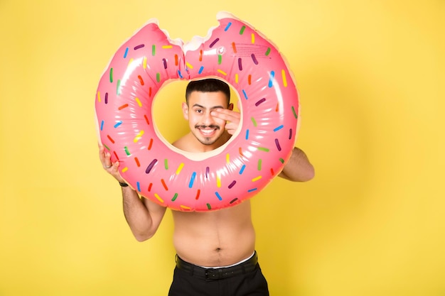 Junger kaukasischer Mann, der einen aufblasbaren Donut hält, isoliert auf gelbem Hintergrund