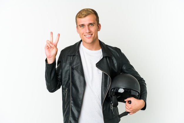 Junger kaukasischer Mann, der einen Motorradhelm lokalisiert auf weißem Raum hält, der Nummer zwei mit den Fingern zeigt.