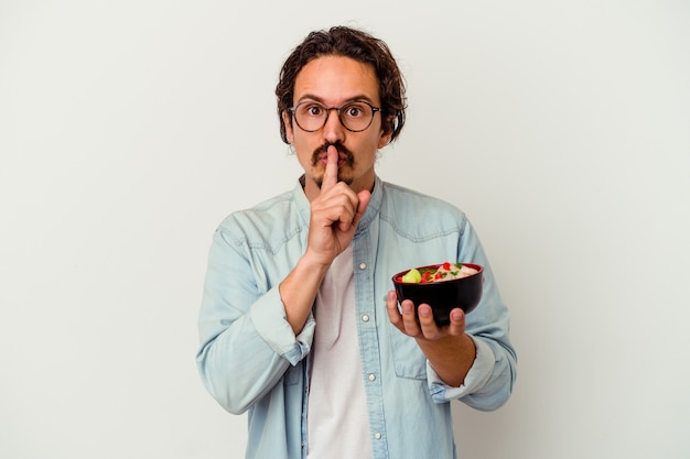 Junger kaukasischer Mann, der einen Ramen isst, der auf weißem Hintergrund lokalisiert wird, der ein Geheimnis hält oder um Stille bittet.