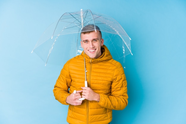 Foto junger kaukasischer mann, der einen regenschirm hält, der lacht und spaß hat.