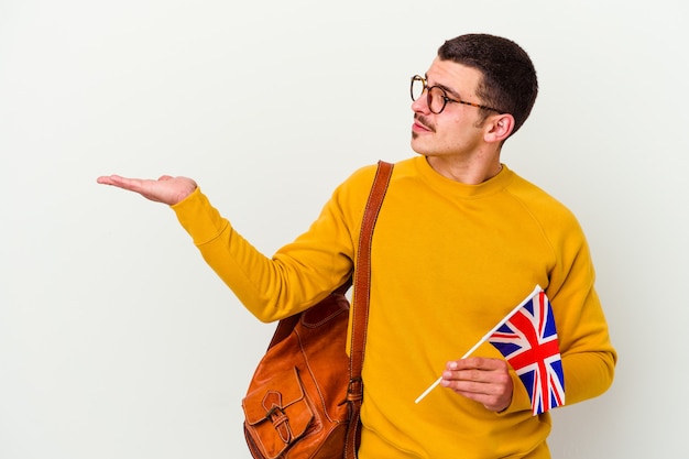 Junger kaukasischer Mann, der Englisch studiert, isoliert auf weißem Hintergrund, der einen Kopienraum auf einer Handfläche zeigt und eine andere Hand auf Taille hält.