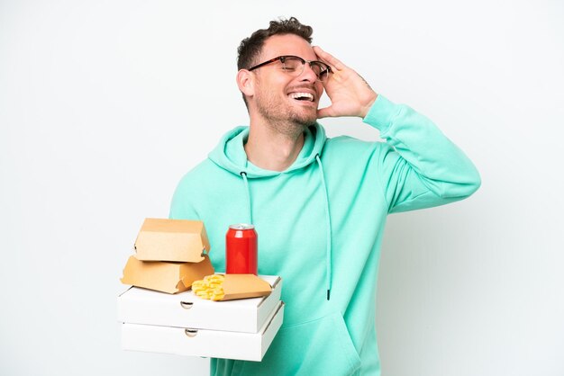 Junger kaukasischer Mann, der Fast Food isoliert auf weißem Hintergrund hält und viel lächelt