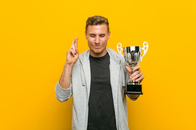 Junger kaukasischer Mann, der Finger einer Trophäenüberfahrt für das Haben des Glücks hält