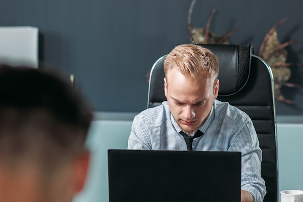 junger kaukasischer Mann, der im Büro mit einem Laptop arbeitet, das Konzept eines Mitarbeiters von European