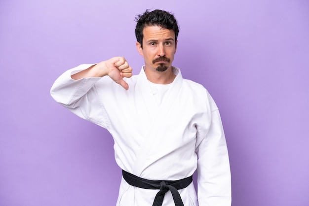 Junger kaukasischer Mann, der Karate macht, isoliert auf violettem Hintergrund, der Daumen nach unten mit negativem Ausdruck zeigt