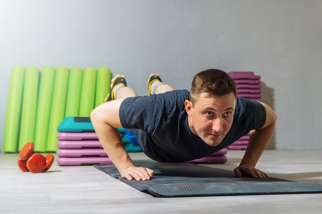 Junger kaukasischer Mann, der Liegestütze auf einer Stufenplattform im Fitnessstudio macht.