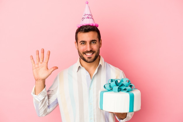 Junger kaukasischer Mann, der seinen Geburtstag feiert, lokalisiert auf rosa Wand lächelnd fröhlich zeigt Nummer fünf mit den Fingern.