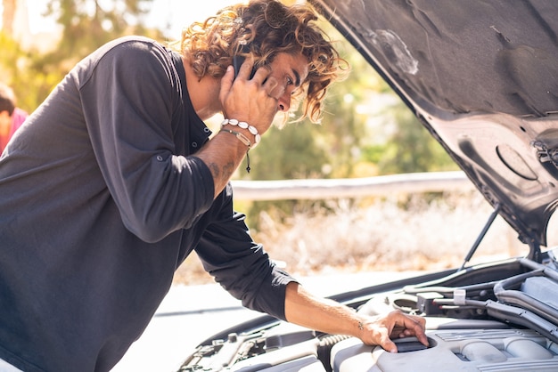 Junger kaukasischer Mann, der versucht, eine Panne in seinem Auto zu reparieren