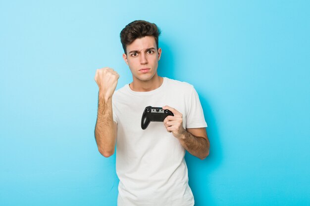 Junger kaukasischer Mann, der Videospiele mit dem Gamecontroller zeigt Faust mit aggressivem Gesichtsausdruck spielt.