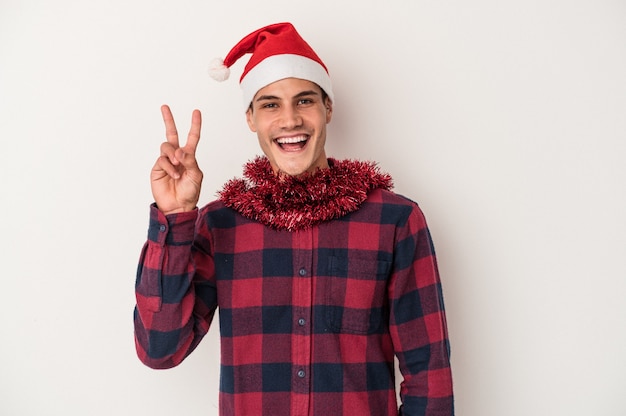 Junger kaukasischer Mann, der Weihnachten isoliert auf weißem Hintergrund feiert, freudig und sorglos, das ein Friedenssymbol mit den Fingern zeigt.