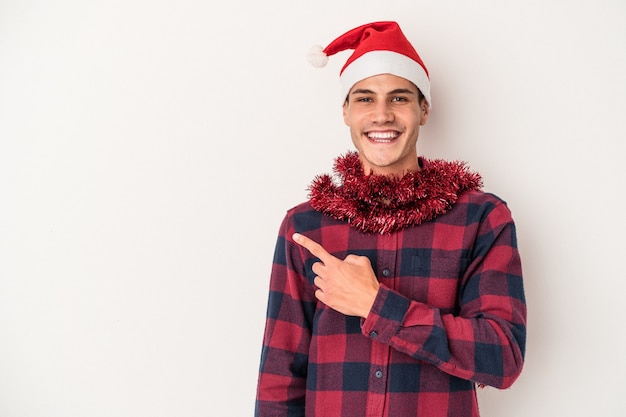 Junger kaukasischer Mann, der Weihnachten isoliert auf weißem Hintergrund feiert und beiseite lächelt und zeigt, etwas an der Leerstelle zeigend.